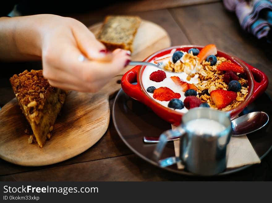 Person Holding Spoon and Round Red Ceramic Bowl With Pastries