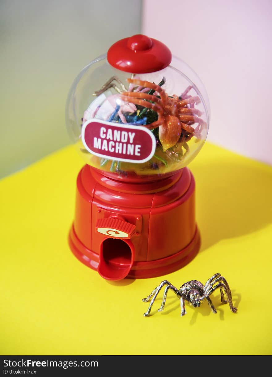 Red and Clear Plastic Candy Machine on Yellow Desk