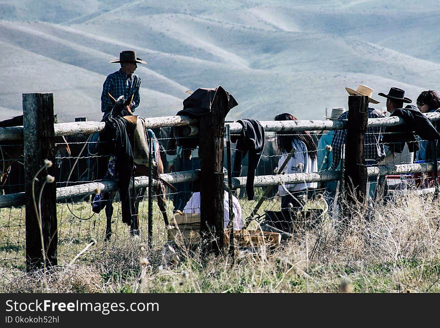 Cowboys Leaning on Brown Fence