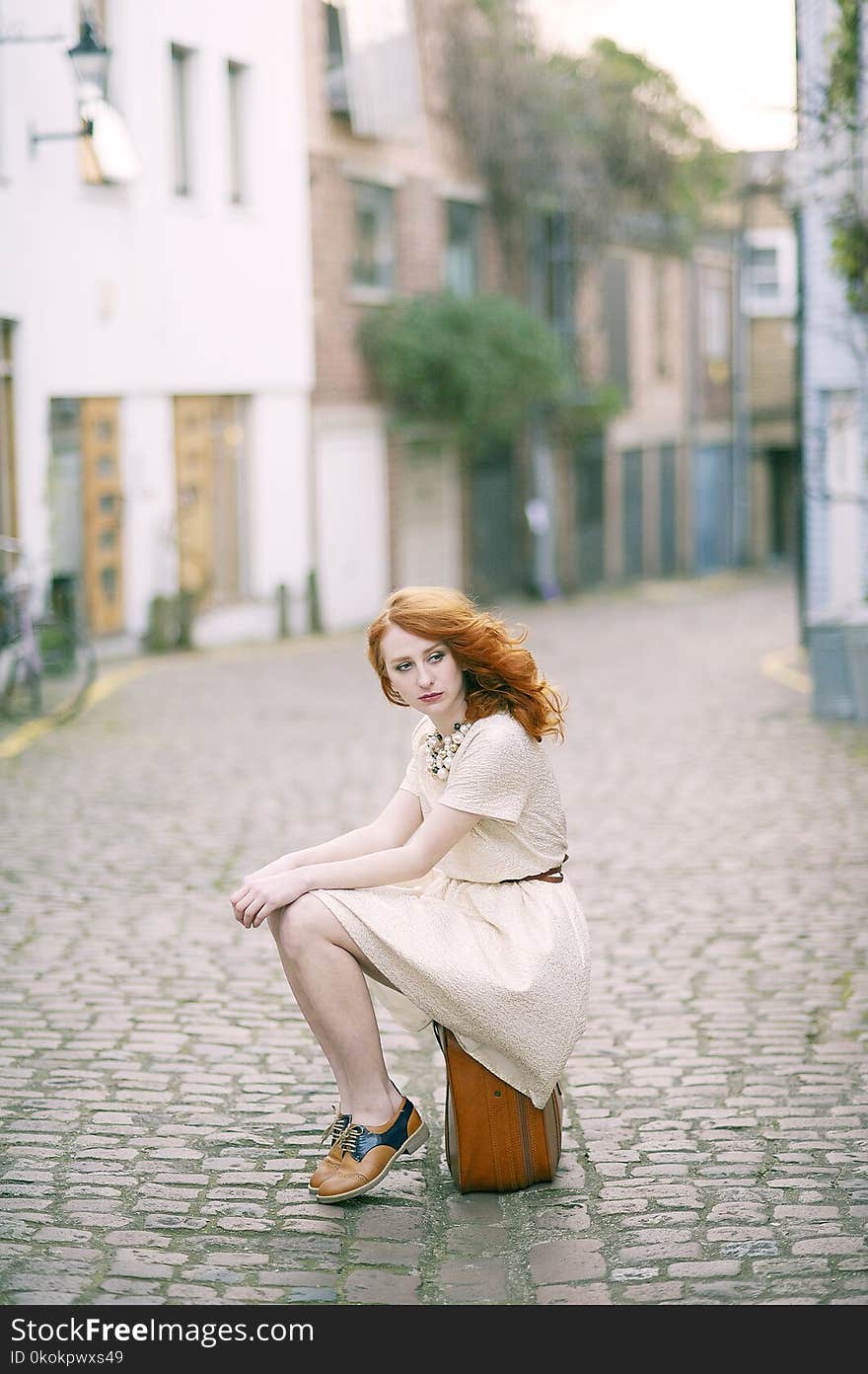 Woman Wearing White Dress Sitting On Brown Lugagge