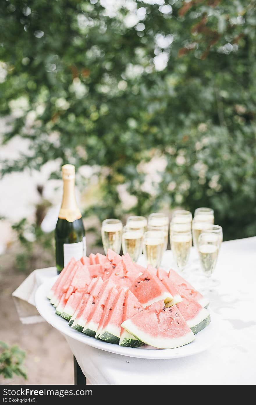 Selective Focus Photo of Bunch of Sliced Watermelons in White Bowl Near Champagne Bottle