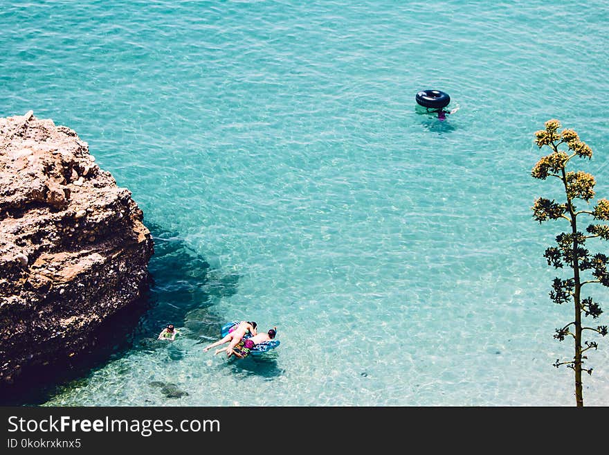 Man and Woman Swimming in the Sea Near Brown Cliff