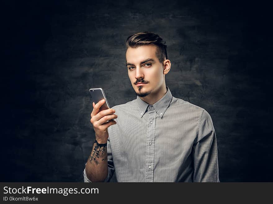 Studio portrait of handsome bearded hipster male with a tattoo on his arm using a smartphone. Studio portrait of handsome bearded hipster male with a tattoo on his arm using a smartphone.