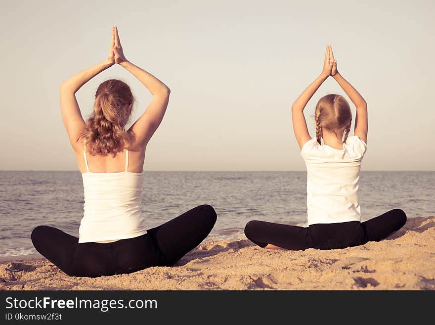 Mother and daughter doing yoga exercises on the beach at the day time. People having fun outdoors. Concept of summer vacation and friendly family. Mother and daughter doing yoga exercises on the beach at the day time. People having fun outdoors. Concept of summer vacation and friendly family.