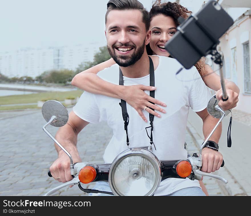 Happy couple on scooter making selfie on smartphone outdoor