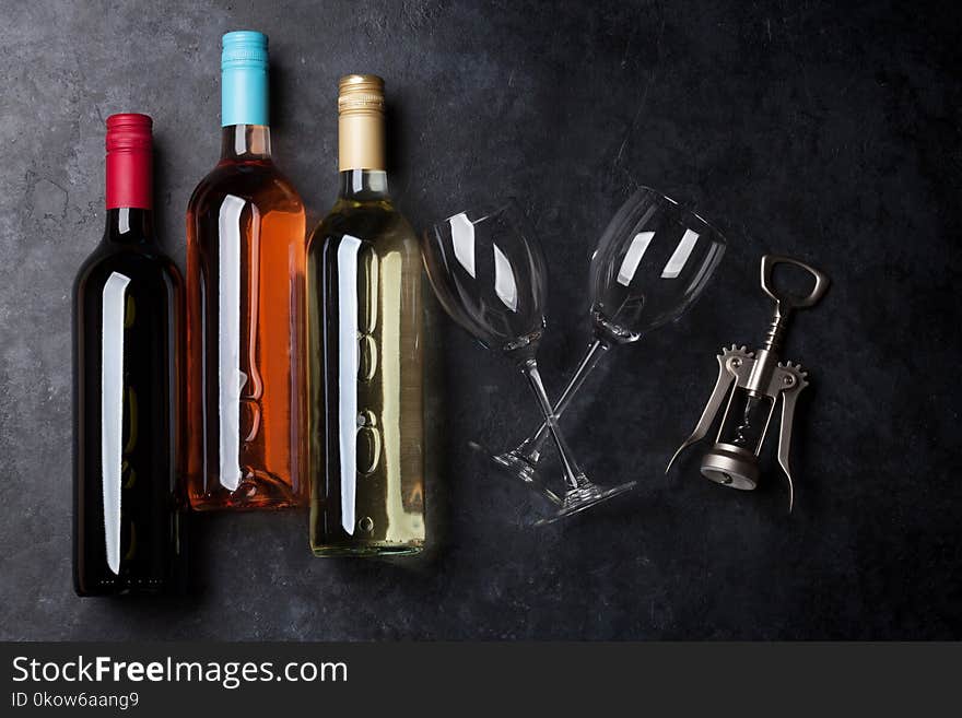 Red, rose and white wine bottles with wine glasses and corkscrew on stone table. Top view