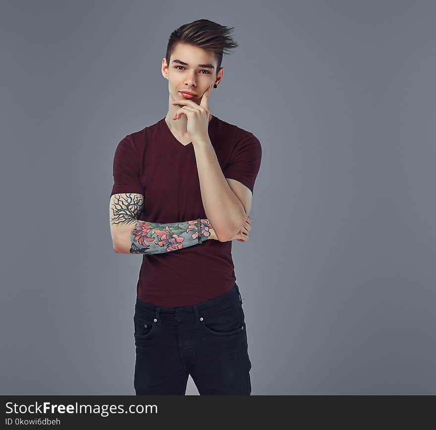 Handsome fashionable pensive guy with stylish hair and tattoo on his arm posing in a studio. on a gray background. Handsome fashionable pensive guy with stylish hair and tattoo on his arm posing in a studio. on a gray background.