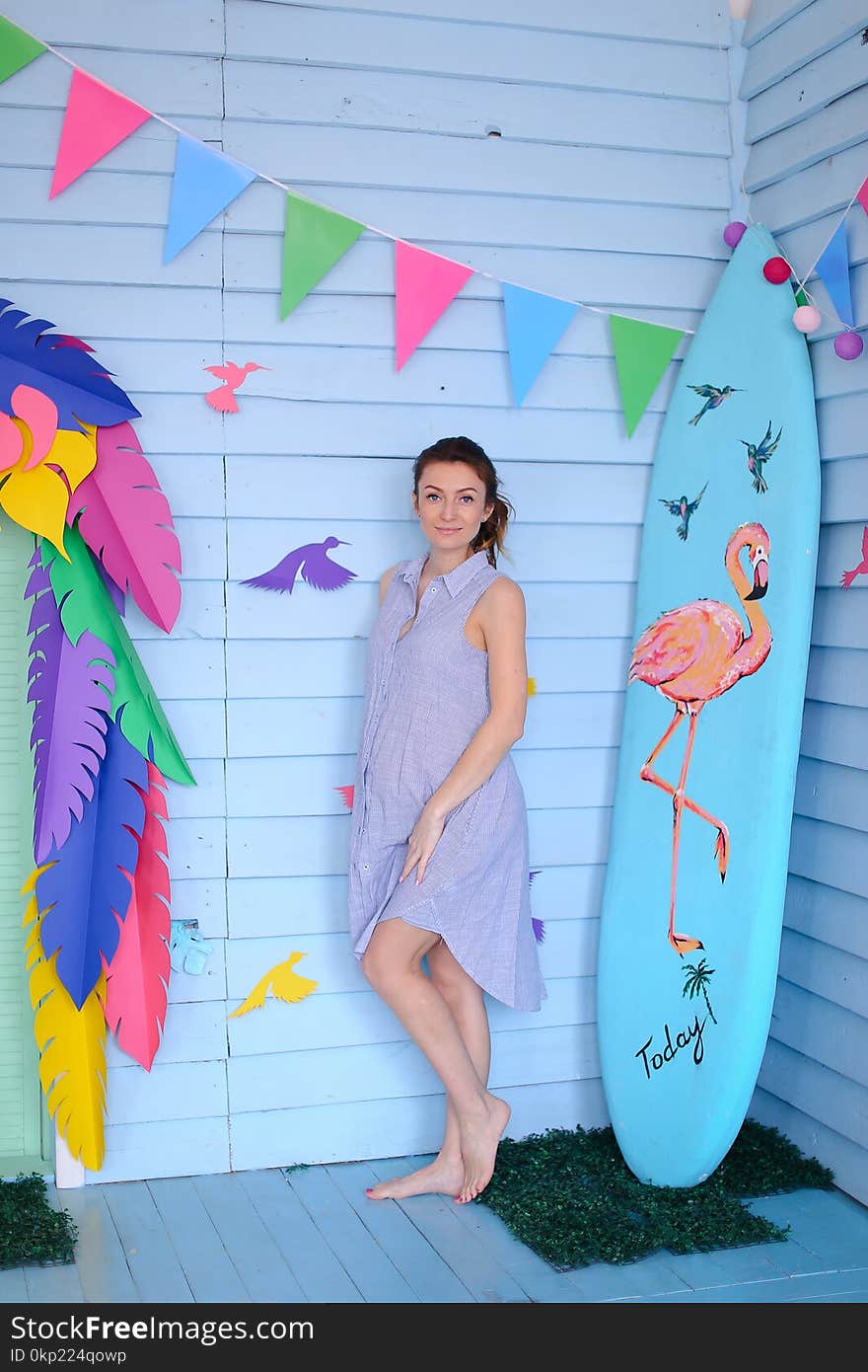Young pretty pregnant woman standing near surfboard and decorated children house. Concept of pregnance and motherhood, summer.