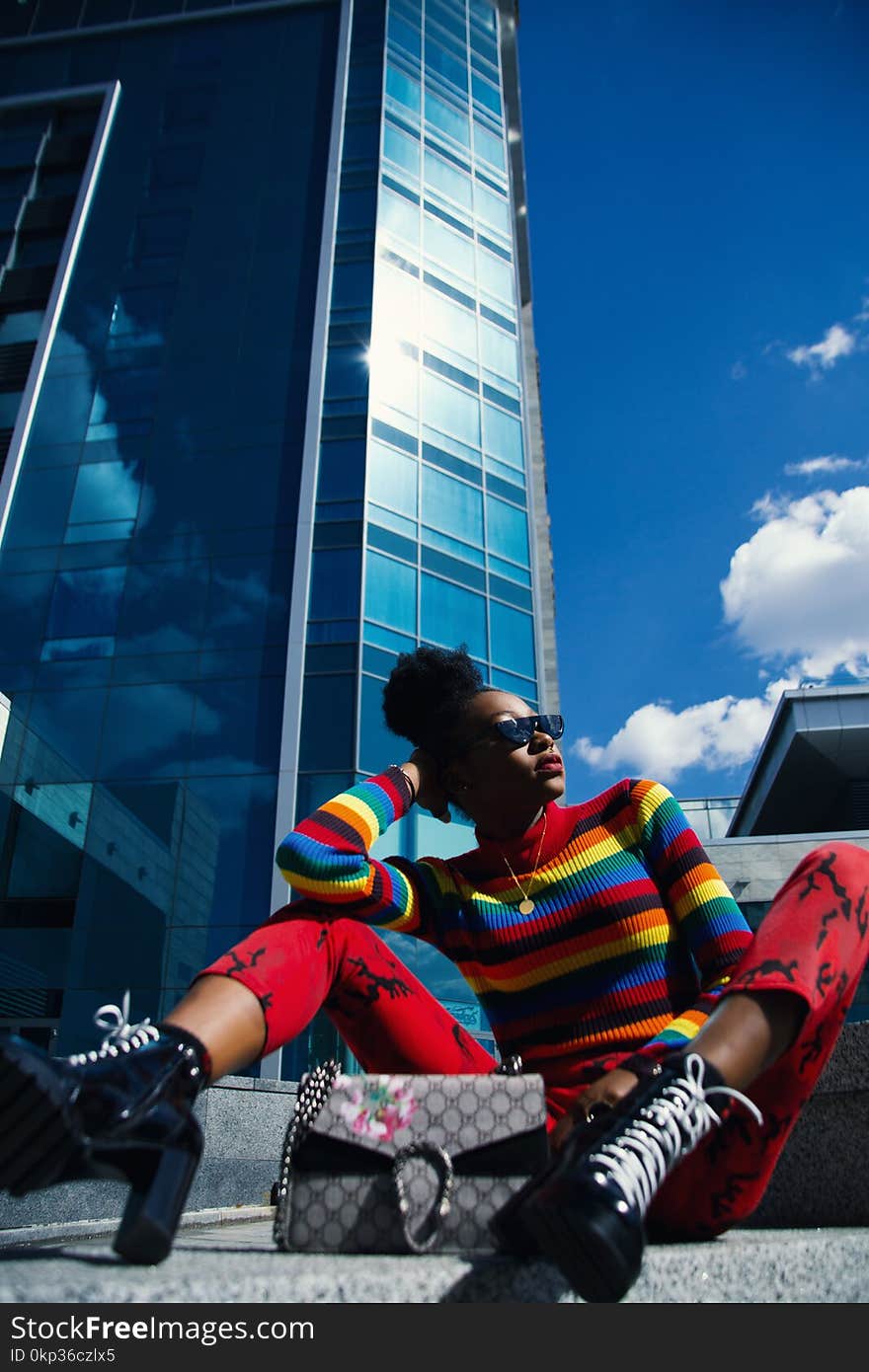 Woman Wearing Blue, Red, and Black Turtle-neck Long-sleeved Shirt and Red Pants Sitting on Ground at Daytime