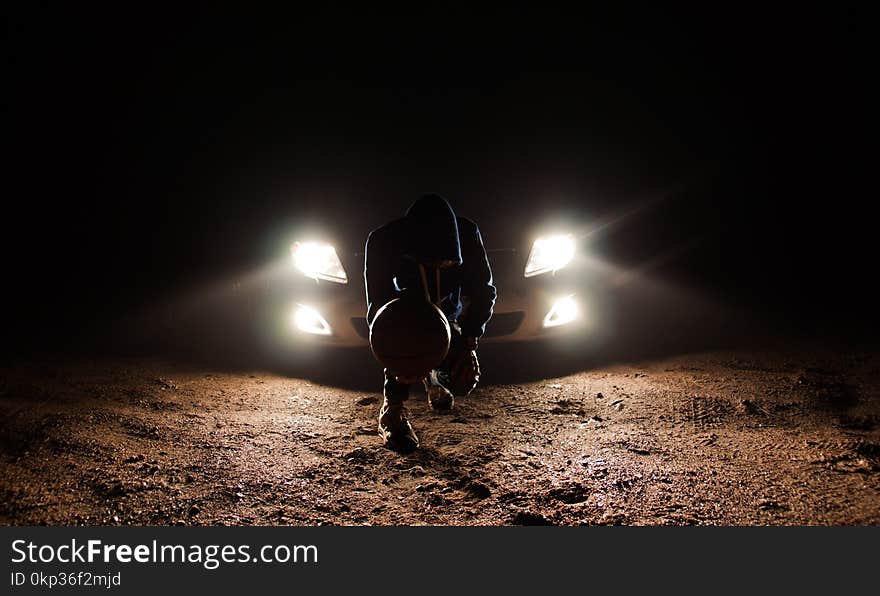 Man Against the Vehicle Headlight Squatting Holding Ball