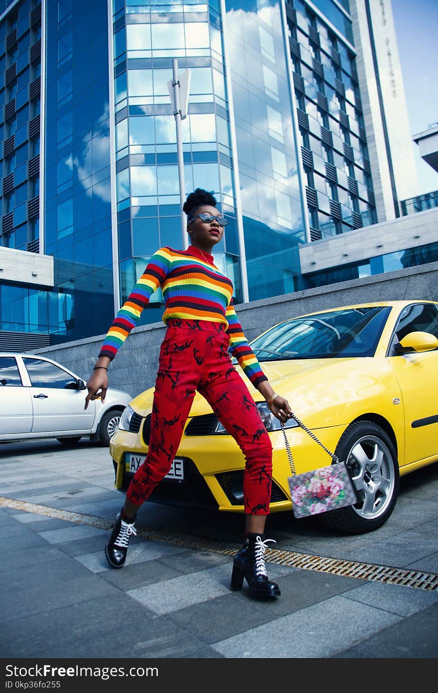 Woman Wearing Multicolored Sweater and Red Denim Jeans Near Yellow Vehicle