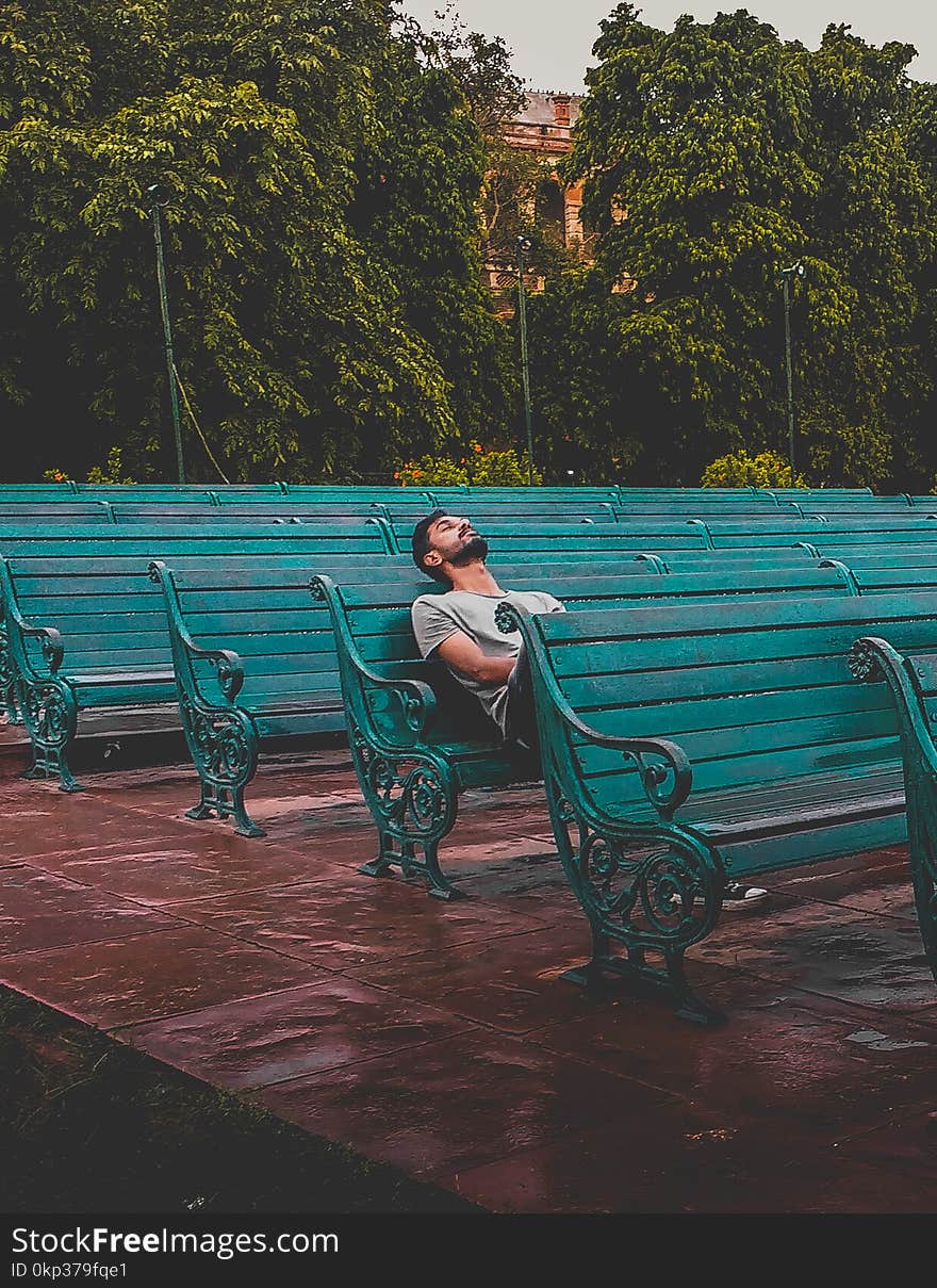 Man Sitting and Closing Eyes on Teal Bench