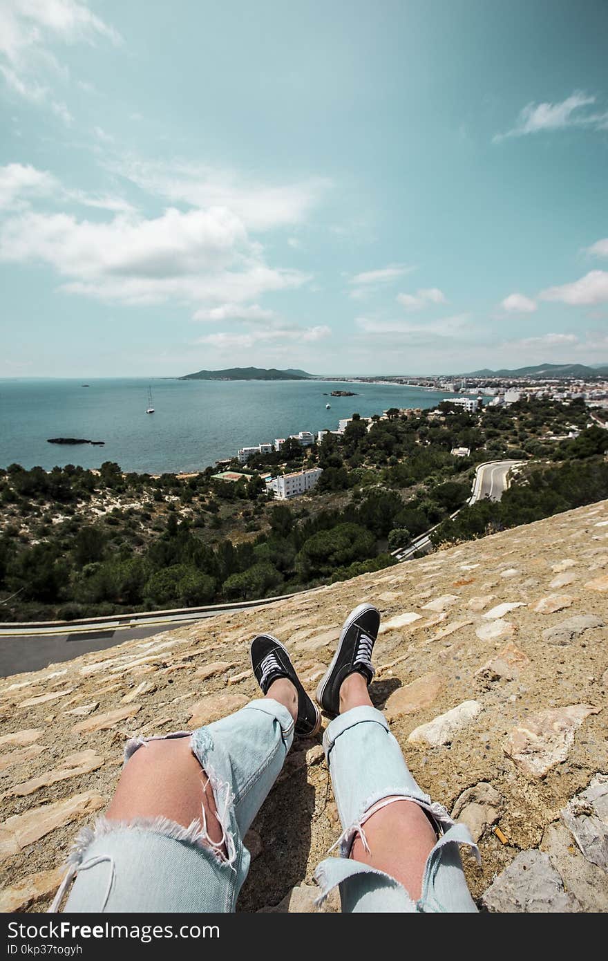 Man in Blue Tattered Jeans Sitting on Top of the Mountain