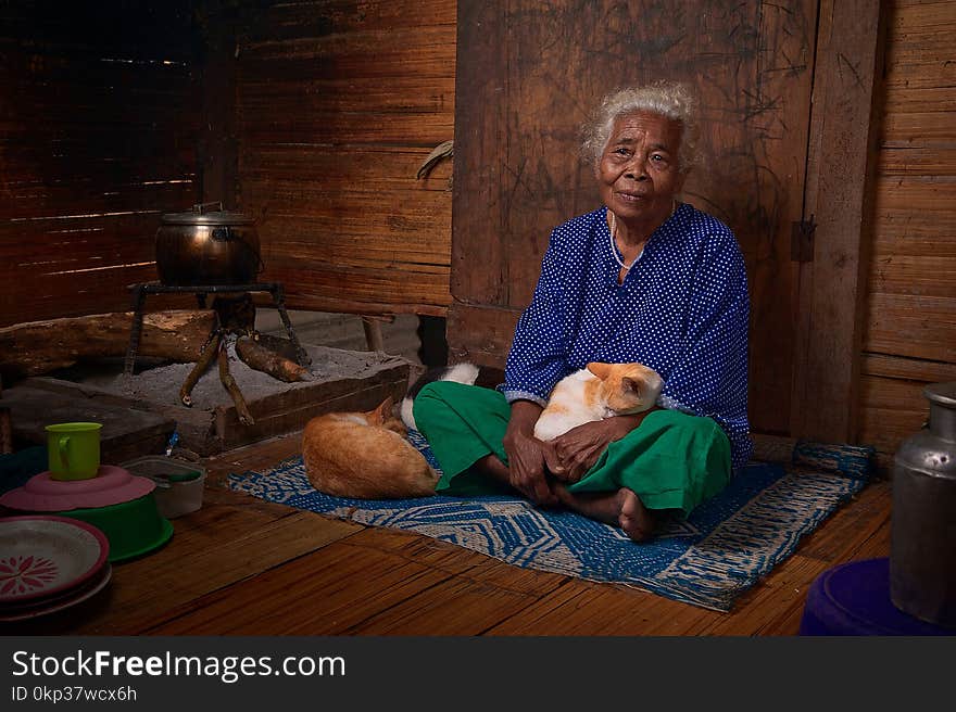 Woman With White Hair In Blue Long-sleeved Top Sitting With White And Orange Tabby Cat