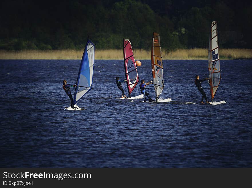 Four Person Riding Wind Sailboard on Body of Water