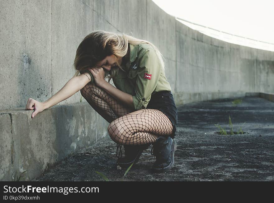 Woman Squatting Near Gray Concrete Wall at Daytime