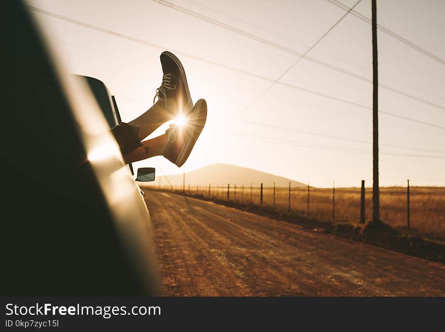 Legs of a woman relaxing at the back of a pick up truck on a highway in country side. Legs hanging out from car with sun in the background. Legs of a woman relaxing at the back of a pick up truck on a highway in country side. Legs hanging out from car with sun in the background.