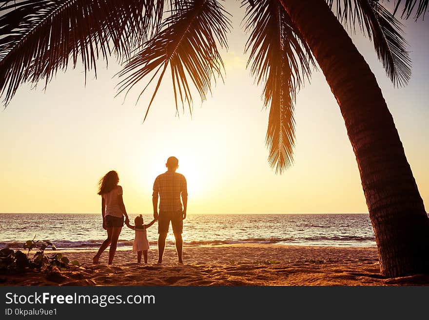 Family with one child stands against sunset sea beach and palms. Tropical vacations concept. Family with one child stands against sunset sea beach and palms. Tropical vacations concept