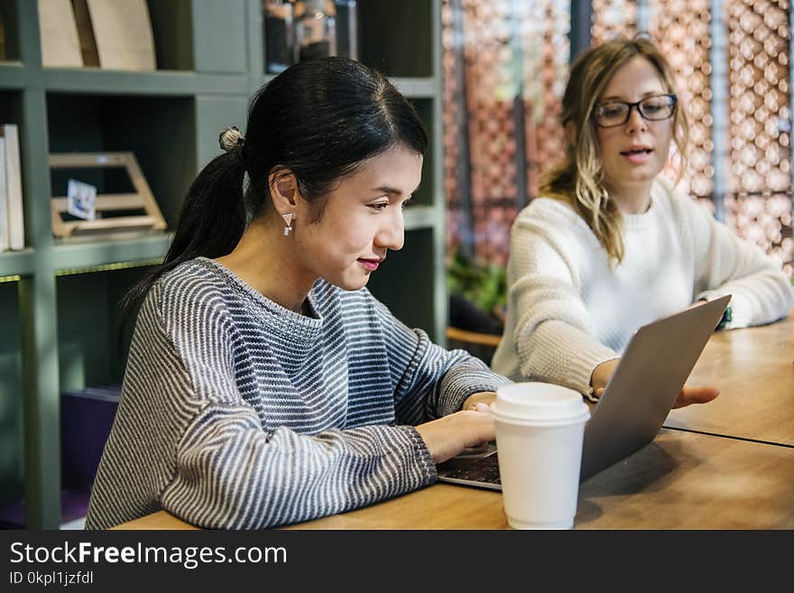 Two Women Sitting In Front Of Brown Wooden Table