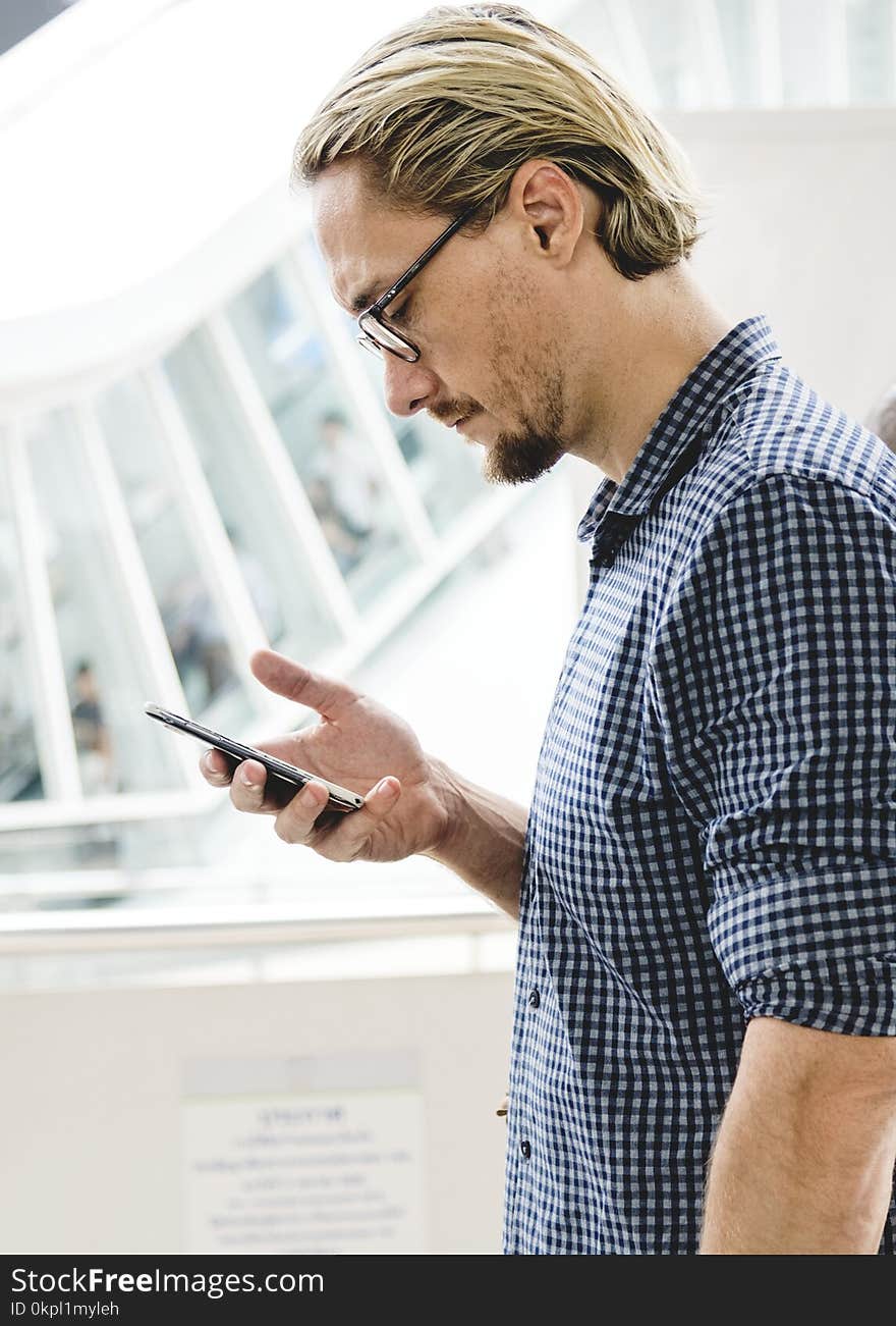 Man in Black and Gray Tattersall Dress Shirt Holding Smartphone