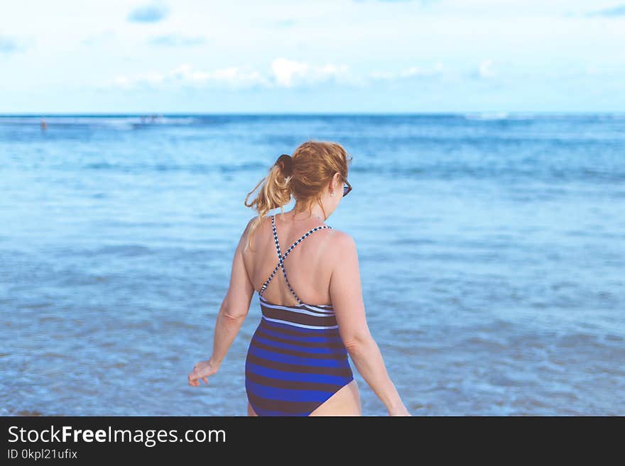 Woman Wearing Blue Monokini Standing Beside Body Of Water Under Blue Sky