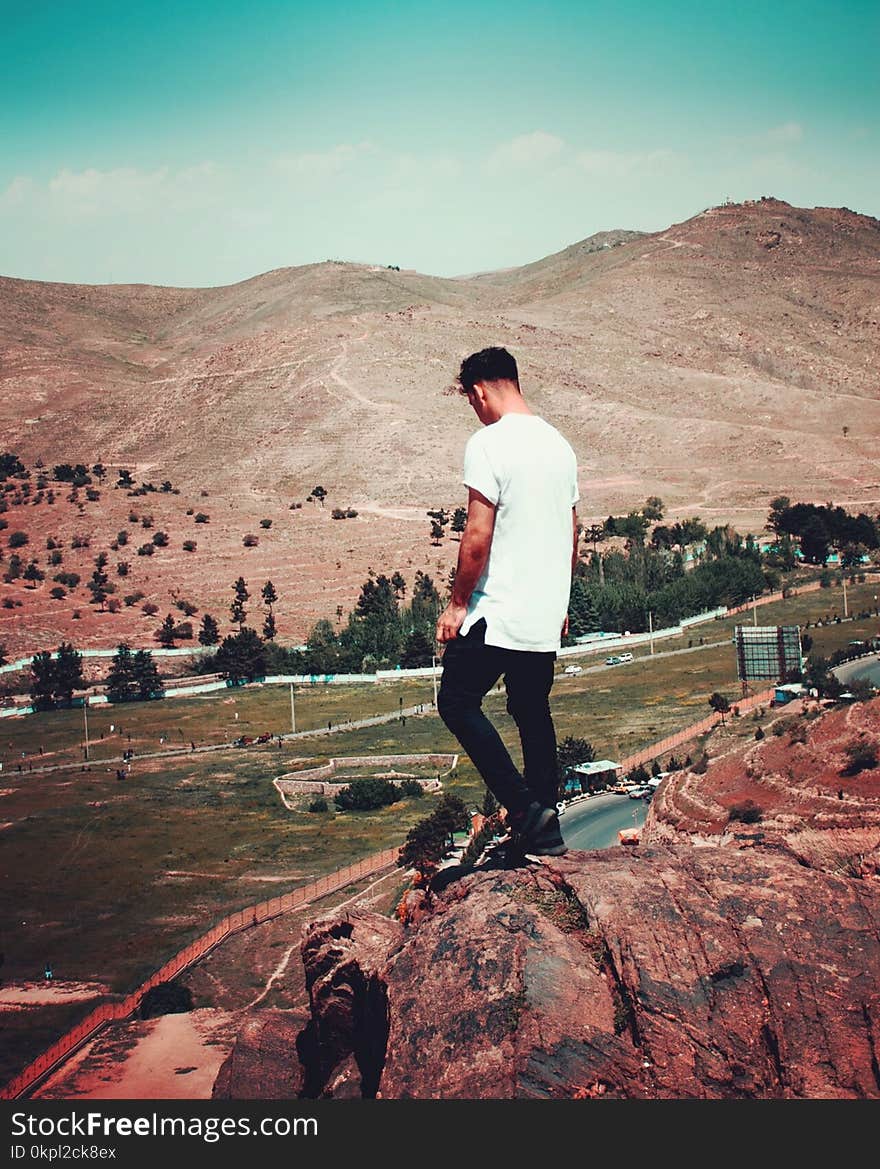 Man in White T-shirt and Black Pants Standing on Cliff