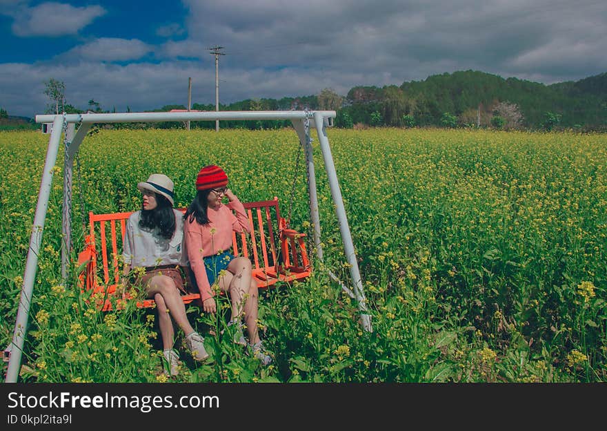 Two Women Sitting On Swing Bench