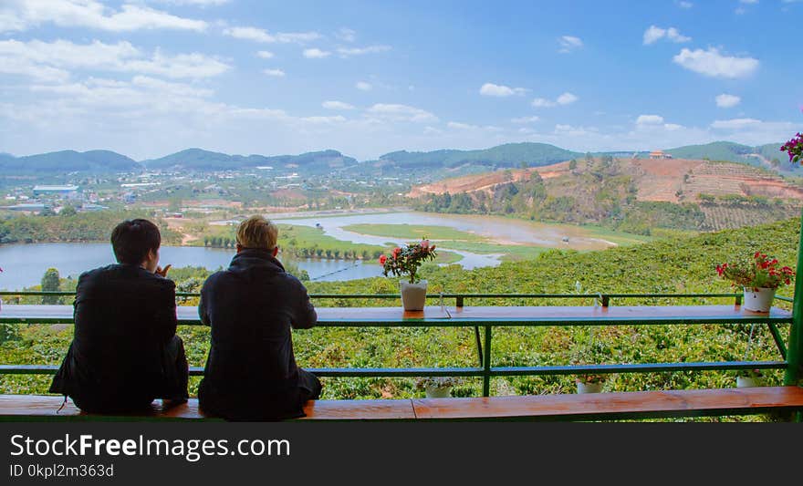 Two Men Sitting On Table Facing Lake