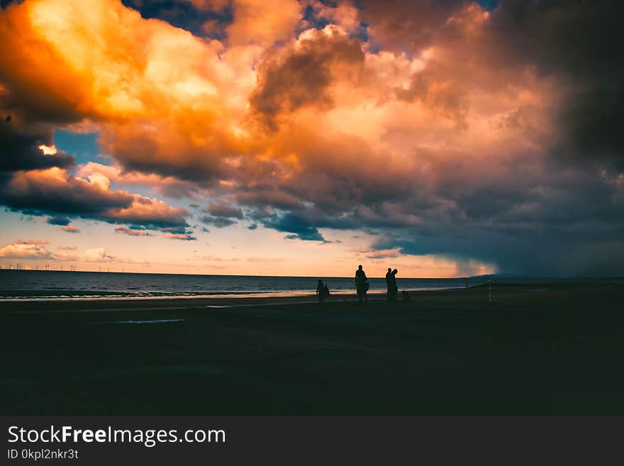 Silhouette Of People On Shore Under Cloudy Sky