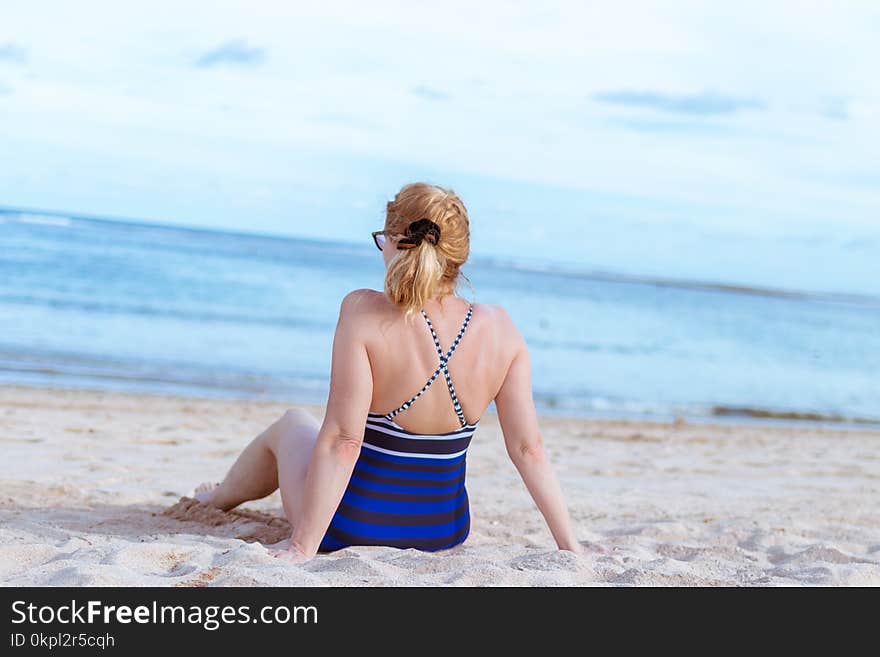 Woman Sits on White Sand Beach