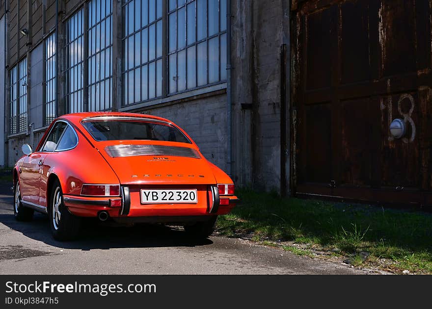 Classic Orange Coupe Near Brown Concrete Building