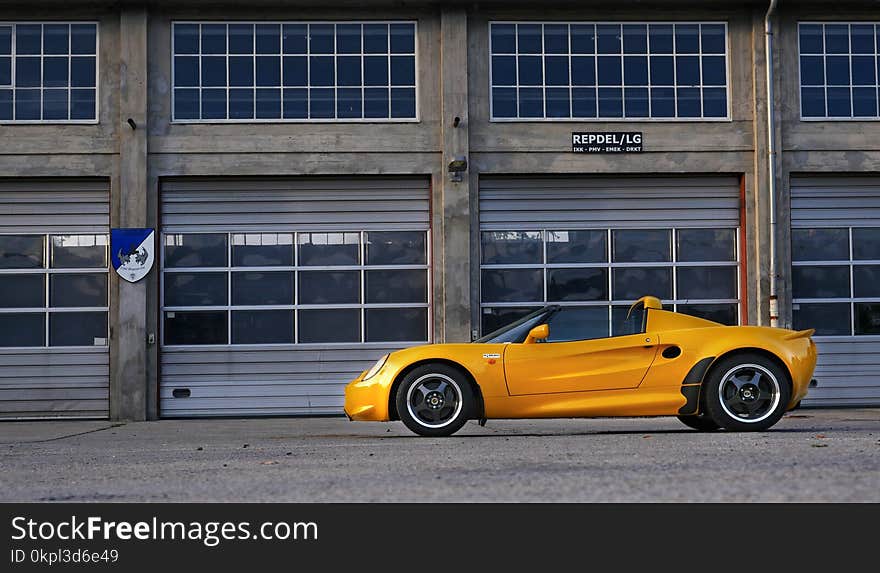 Yellow Coupe Parked Near Brown Painted Warehouse