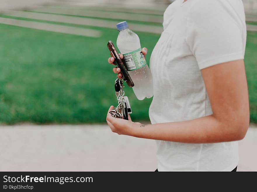 Person Holding Key, Smartphone, And Plastic Bottle