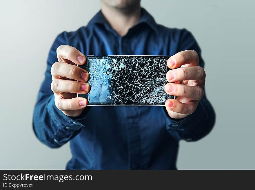 Bearded upset man holds a out-of-use tablet or smartphone. on a light background. Broken screen