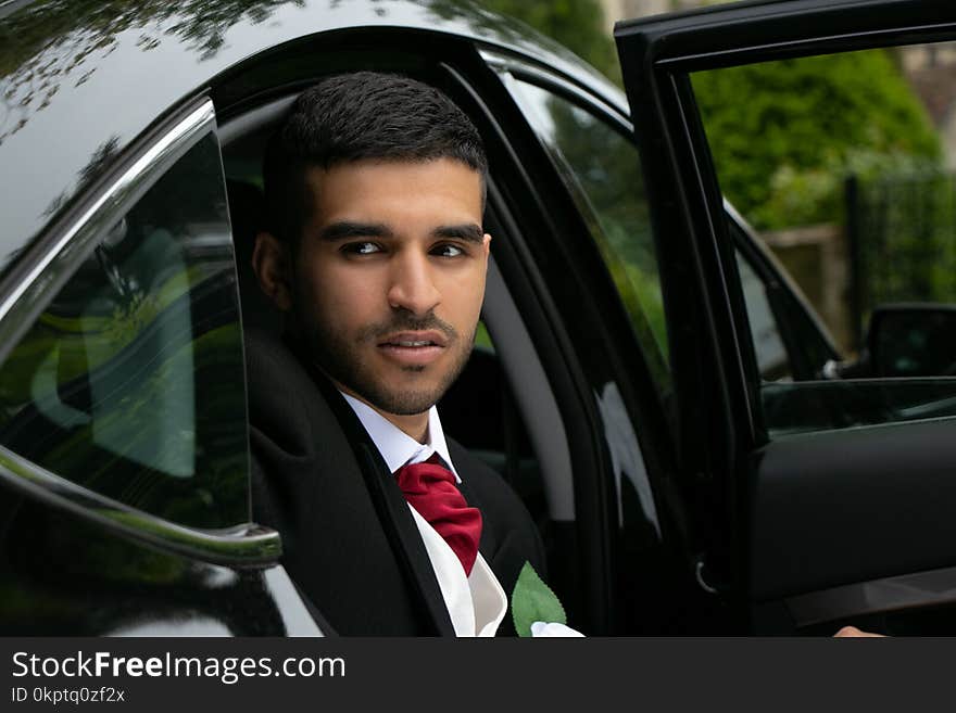 Groom arrives at church on his wedding day by car and poses for pictures next to car outside of village church. Groom arrives at church on his wedding day by car and poses for pictures next to car outside of village church.