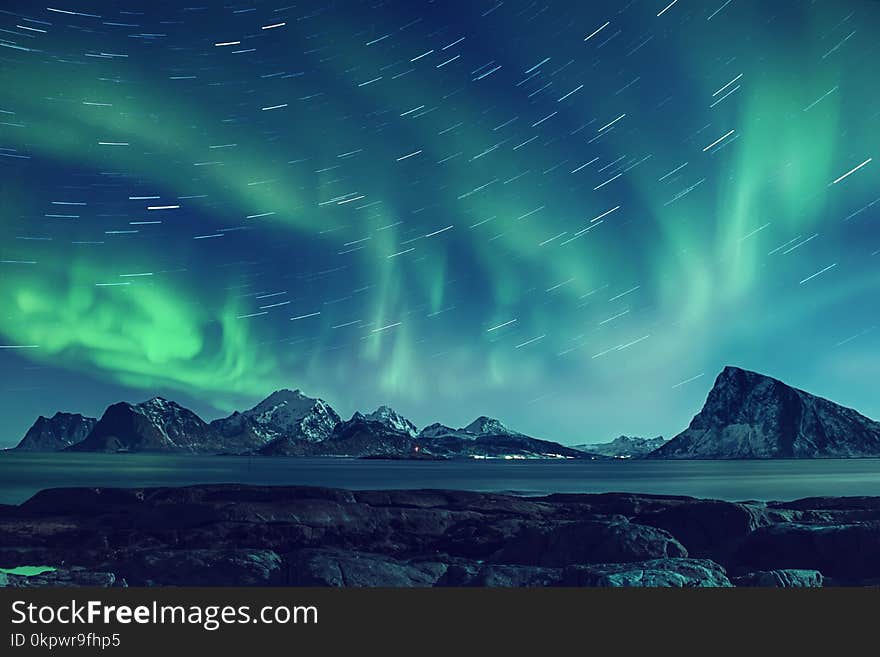 Northern Lights, Aurora Borealis shining green in night starry sky with star tracks at winter Lofoten Islands, Norway. Northern Lights, Aurora Borealis shining green in night starry sky with star tracks at winter Lofoten Islands, Norway