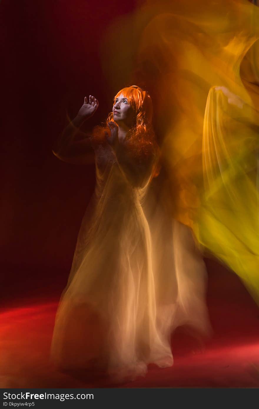 Old female actress with orange hair dancing in white dress with light show with yellow, orange and green lights around