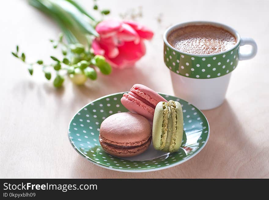 Spring coffee background. Pink tulip, freesia, espresso and macarons in front, spring flowers in the back.