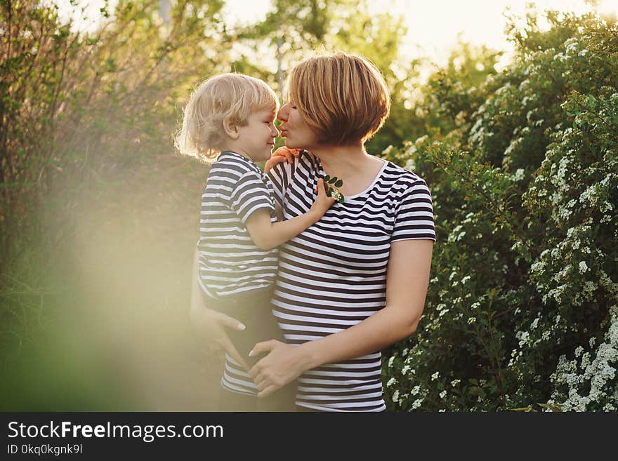 Mother and son in striped T-shirts. Woman holds boy in her arms and kisses him in nose. Family time. Mother and son in striped T-shirts. Woman holds boy in her arms and kisses him in nose. Family time