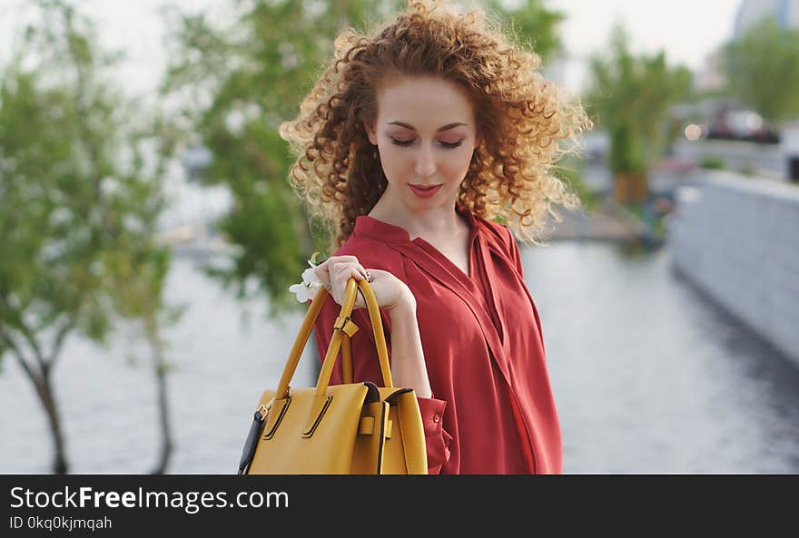 Girl with curly hair. She holds handbag in her hand and poses against background of river and flooded trees on waterfront. Springtime. Girl with curly hair. She holds handbag in her hand and poses against background of river and flooded trees on waterfront. Springtime.