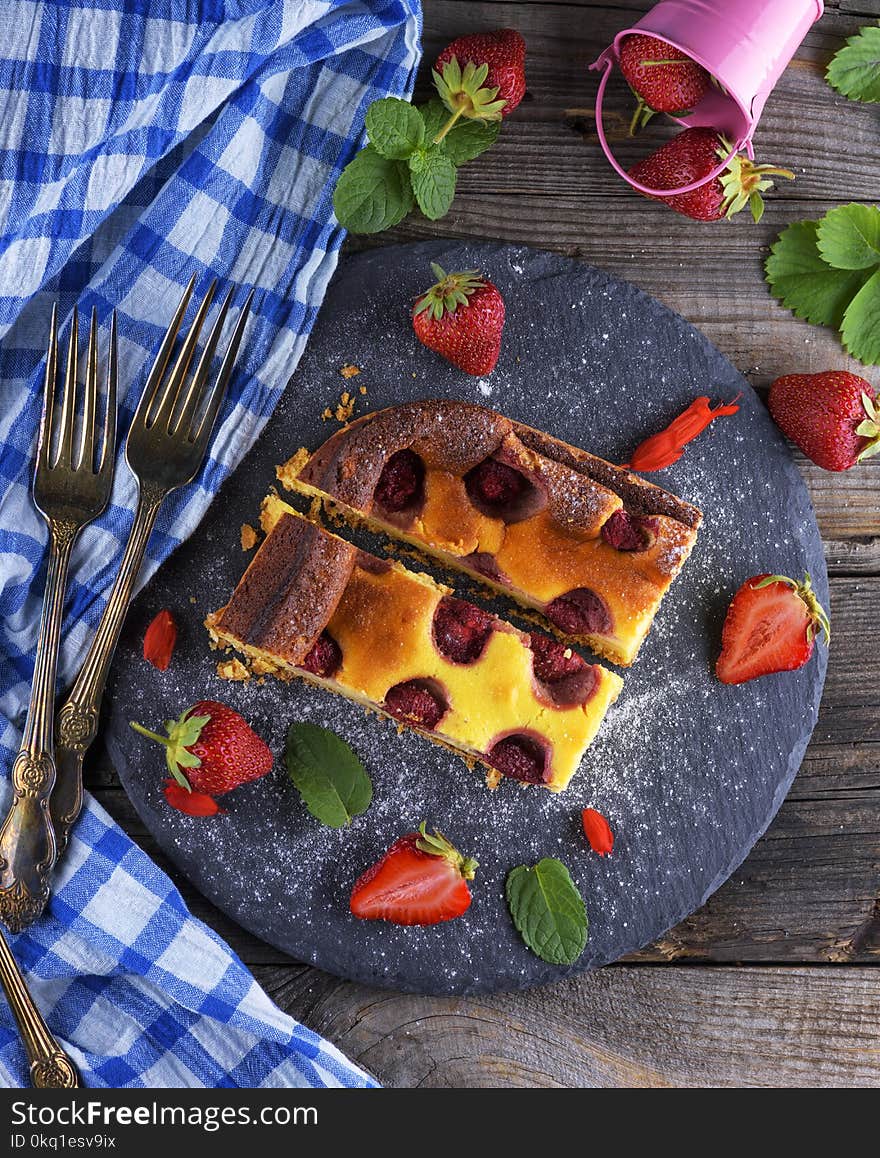 Two pieces of cheesecake with strawberries on a black graphite plate, top view, next to fresh ripe berries