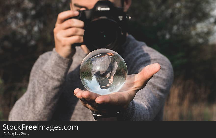 Man Wearing Space-dyed Sweater Holding Water Globe While Holding Black Canon Camera