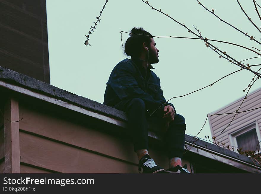 Man Wearing Black Jacket With Black Pants Sitting on Roof at Daytime