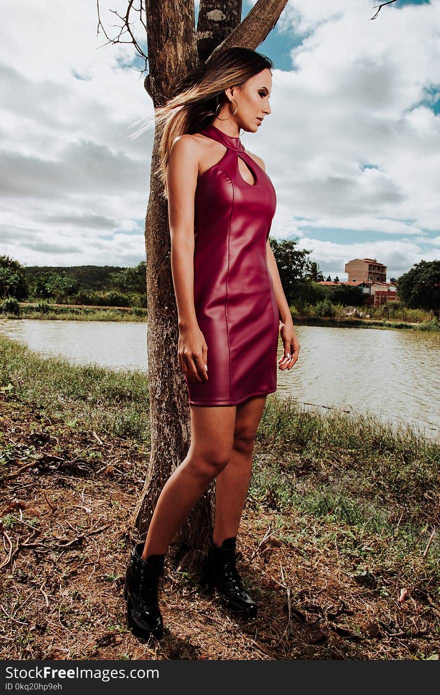 Woman in Red Leather Halter Keyhole Midi Dress Leaning on Brown Tree