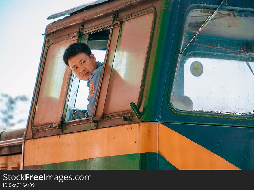 Man Wearing Blue Shirt Driving Green and Yellow Vehicle