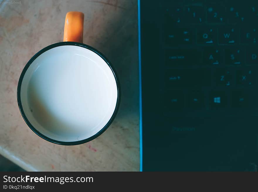 Orange and Black Ceramic Mug With Milk Beside Black Laptop