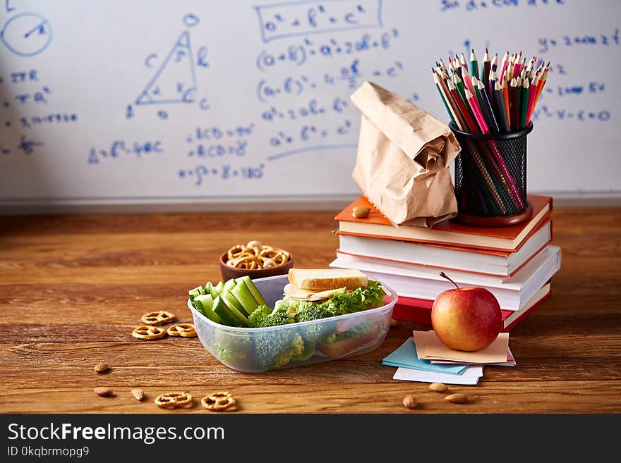 Back to School concept, school supplies, biscuits, packed lunch and lunchbox over white chalkboard, selective focus.