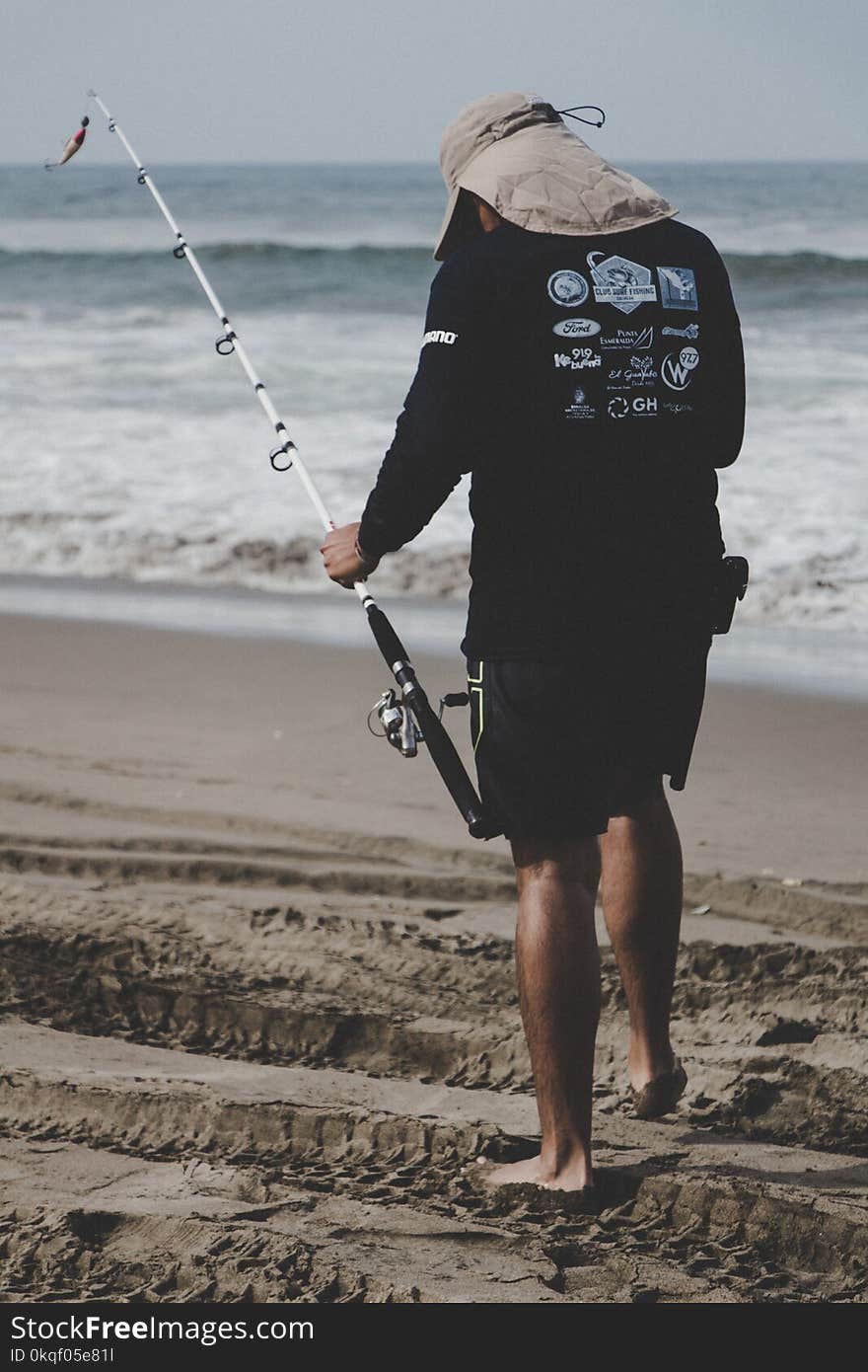 Man in Black Long-sleeved Top Holding White Fishing Rod Near Beach