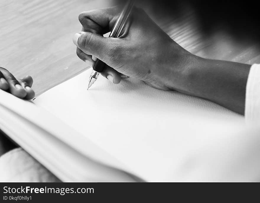 Grayscale Photography of a Person Holding Ball Point Pen Writing on White Notebook Page