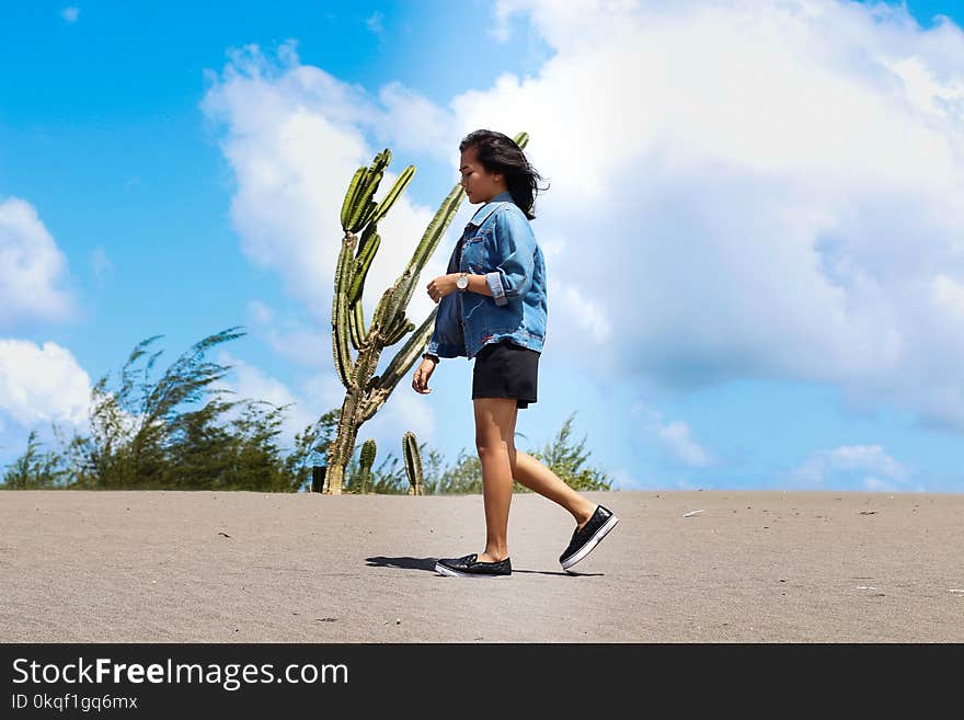 Woman Wearing Chambray Jacket and Black Shorts Walking on Sand Near a Cactus at Daytime